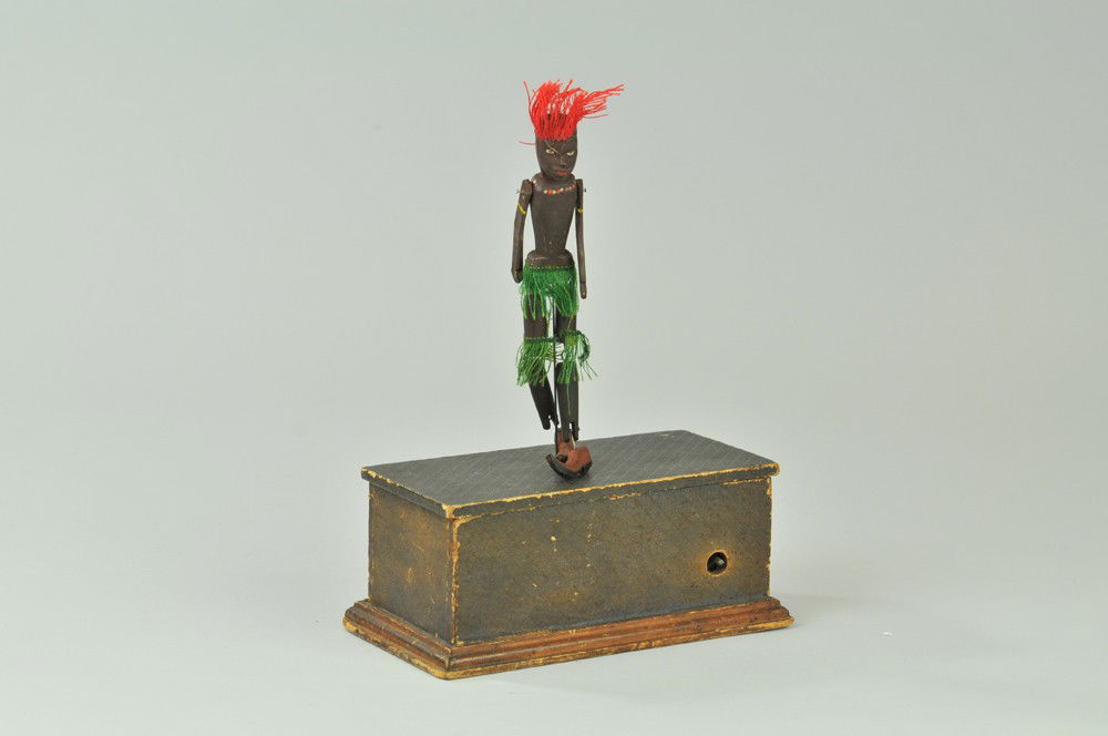 AUTOMATIC TOY WORKS DANCER ON BOX: Paper label on inside says, Perry and Co.'s, Automation Dancers. Figure and box are wood, figure trimmed in cloth outfit with head dress, working well. 10" l. Wear to stage edges, (VG Cond) 10" l.