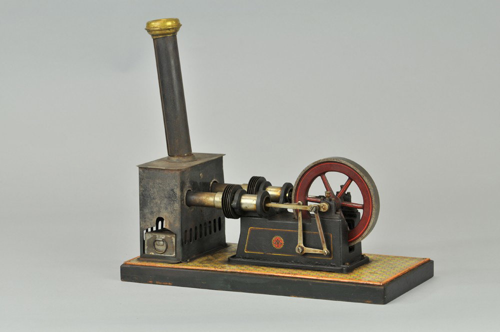 CARETTE STEAM ENGINE: Germany, interesting design, rectangular fire box and boiler, activates twin cylinders by flywheel on raised platform, litho tin base. 13" l. x 11" h. (Good Cond) 13" l. x 11" h.