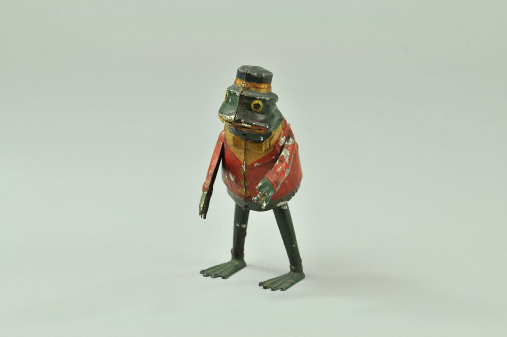 PERFORMING FROG: Germany, hand painted tin, whimsical suited frog with hat and cane in hand, done in red and green, clockwork activated motions. 7" x 2 1/2". Right arm repainted. (VG Cond.) 7" x 2 1/2".