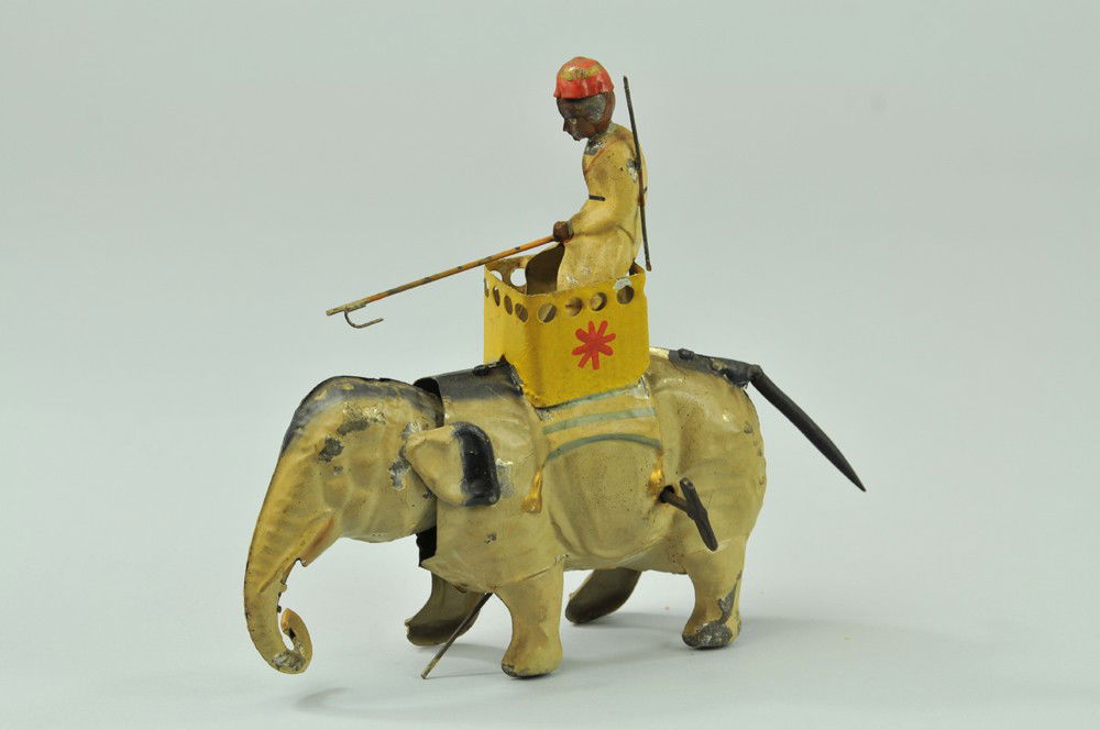 ELEPHANT WITH RIDER IN HOWDAH: Gunthermann, hand painted tin elephant with clockwork mechanism allowing elephant's neck to move forward, rider depicted with bull stick in hand, the elephant's tail is a long spiral spring. 6 1/4" l.