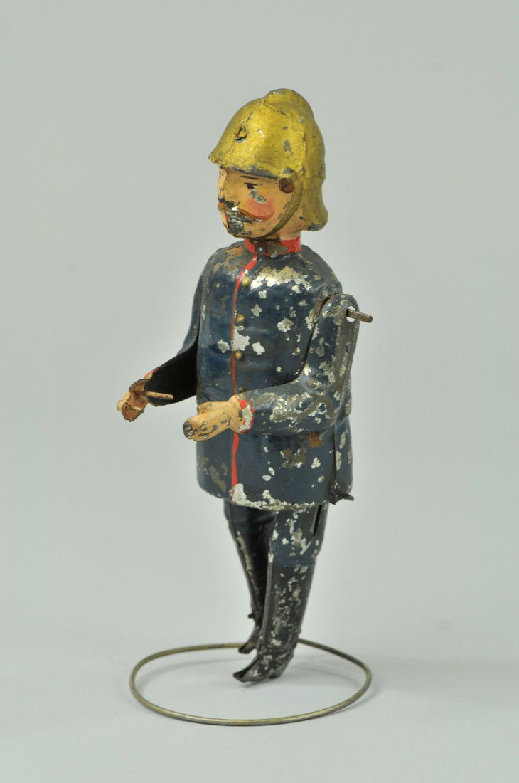 GERMAN FIREMAN: Attributed to Gunthermann, hand painted tin figure, hands contain spikes to allow climbing of ladders, clockwork action. 7 1/4" l. Scratches to litho, missing ladder, paint flaking. (Good Cond.) 7 1/4