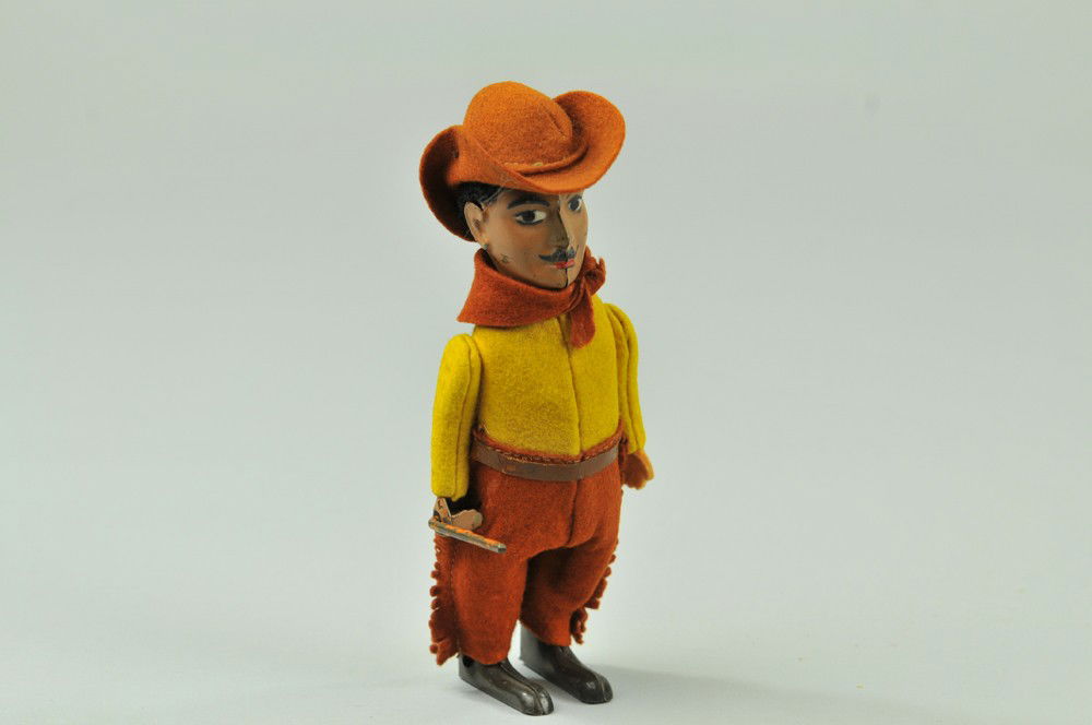 SCHUCO COWBOY: Tin body, clockwork figure has flock covered face, moustache, dressed in yellow shirt, brown felt cowboy style trousers, brown felt kerchief, holds stick in right hand, black closed feet, clockwork ac