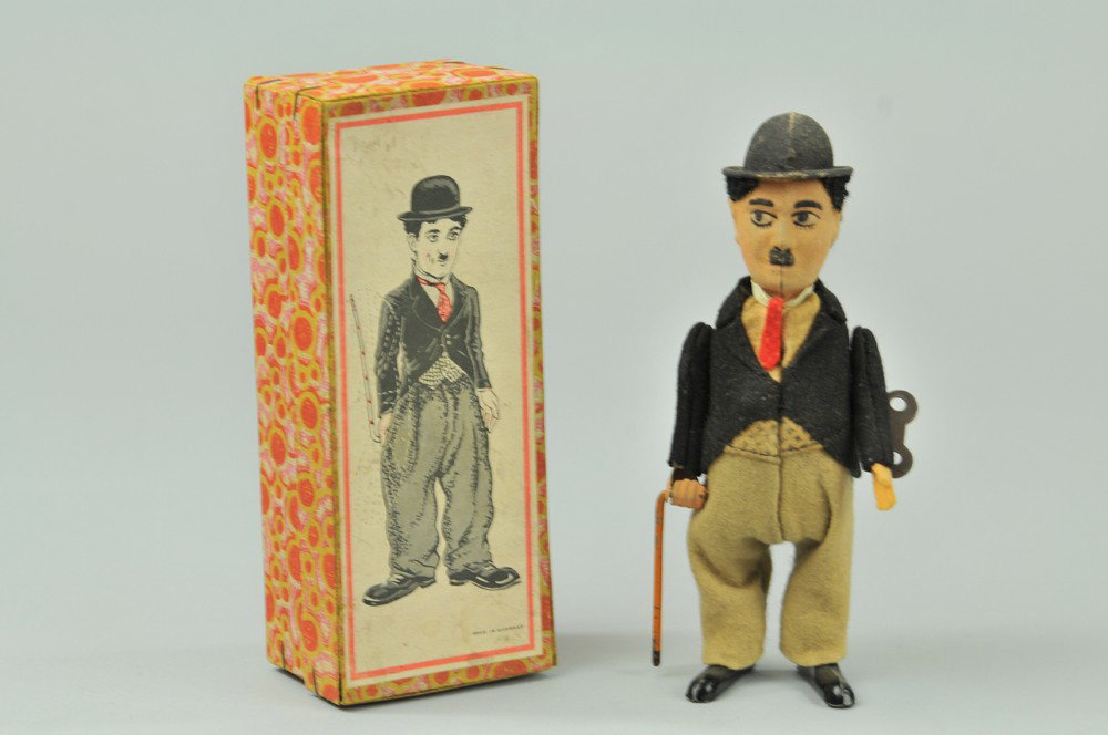 CHARLIE CHAPLIN WALKING FIGURE: Germany, boxed example, tin body, wears felt suit and hat, figure depicted with black woven hair, holds cane in hand, clockwork activated. 6 1/2" h. Tears to box lid, one arm loose, otherwise (VG Cond