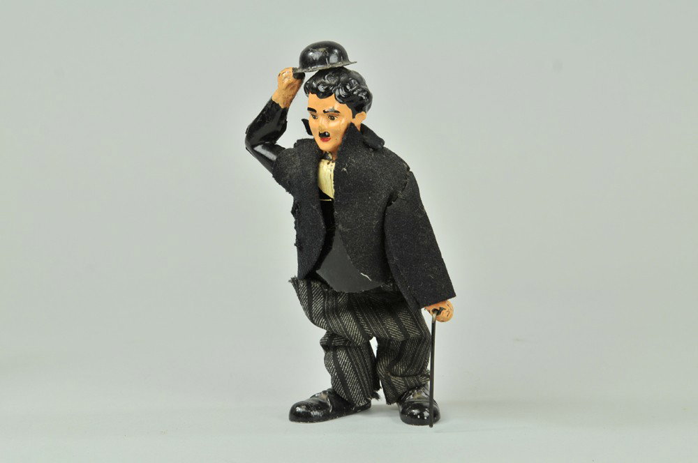 CHARLIE CHAPLIN TOY: Possibly German mfg., hand painted tin figure, depicted in classic attire, hat in hand, cane in one hand, clockwork activated waddling motions, tin body, wire legs, lead shoes. 8" h. Redressed with to
