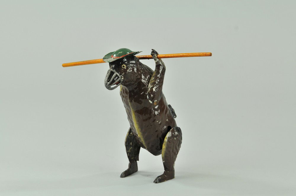 PERFORMING BEAR TOY: Germany, hand painted tin, holds bar at neck, wears muzzle and green hat, amusing clockwork action, possibly Gunthermann. 6 1/2" h. Replaced pole. Toy - (Exc. Cond) 6 1/2" h.
