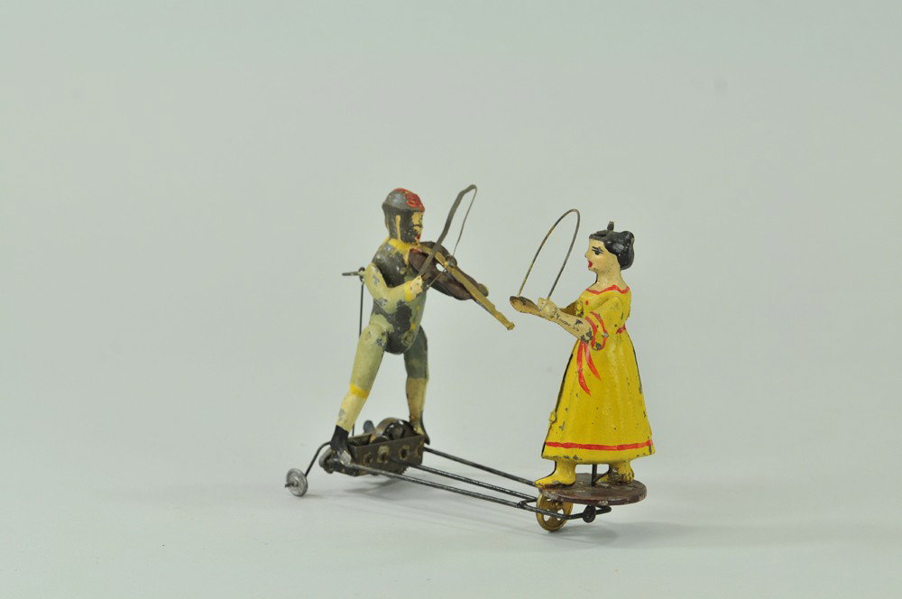 GUNTHERMANN FIDDLER & DANCER: Hand painted tin, key wind appears under fiddler, varied actions, fiddler plays as girl spins. 6 1/2" h. Paint flaking. (Good Cond) 6 1/2" h.