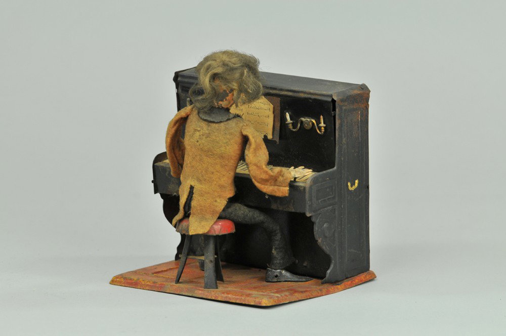 MARTIN PIANO PLAYER: France, very well detailed toy, features cloth dressed musician seated at tin piano with candles and music sheet, clockwork mechanism. 5 1/8" h. Piano base and top tab broken off, clothes stained, key