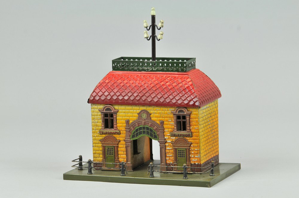BING RAILROAD TELEGRAPH STATION: c. 1915, embossed tin station house, main walkway, red roof, telegraph pole on roof, railed base. 9" x 6". Some wear and minor corrosion. 9" x 6".