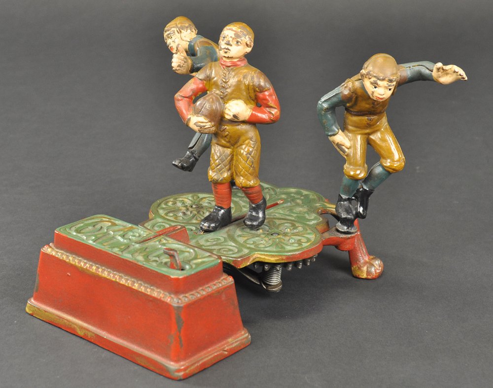 CALAMITY MECHANICAL BANK: J & E Stevens Co., designed by James H. Bowen, patented 7/30/1904. Move the right and left tackles back to position, place a coin in the slot in front of the Full Back and press lever. As the players 