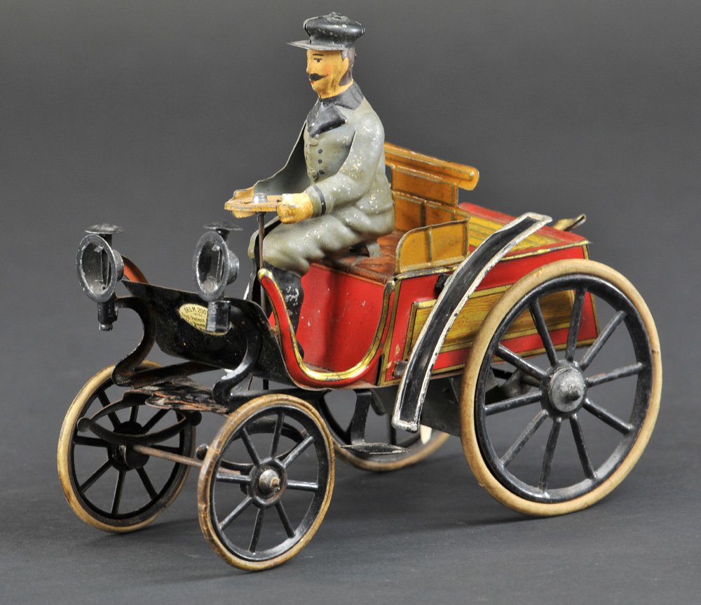 GUNTHERMANN VIS-À-VIS: Germany, c. 1895, open auto w/hand painted seated figure, lithographed tin body done in reds, head lamps on curved hood, rubber tires, spoke wheels. 6 1/2" l.