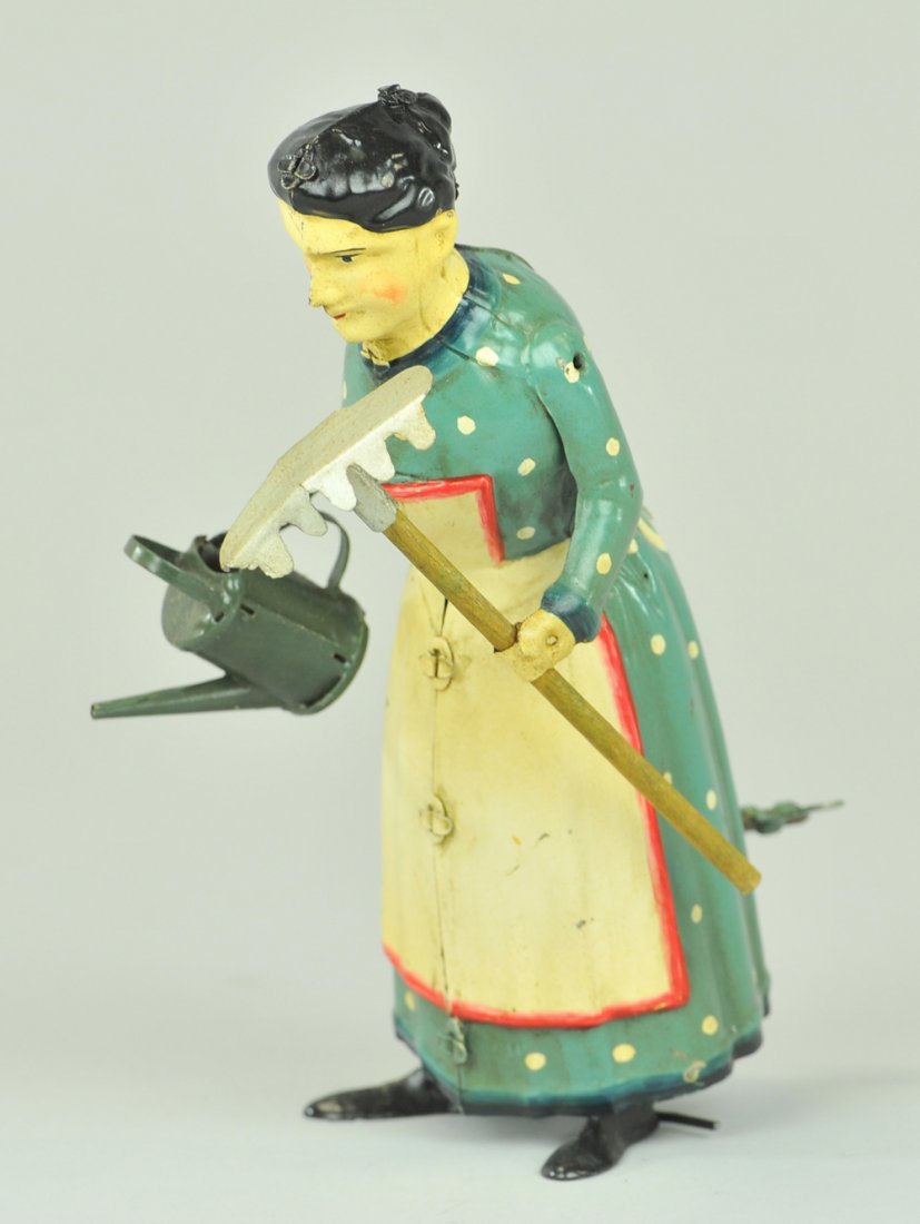 GARDENING LADY WITH RAKE: Hand painted tin, clockwork activated, lady walks carrying watering can and rake, very amusing & novel toy. 7 1/2" h.
