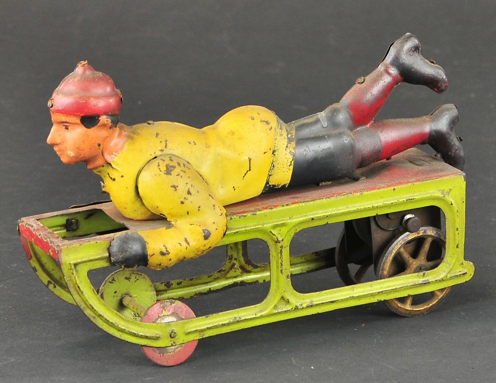 DAYTON BOY ON SLED: Pressed steel, friction driven, colorful example in multi-painted clothes, green sled, depicted with hands on sides, legs in air. 9" l.