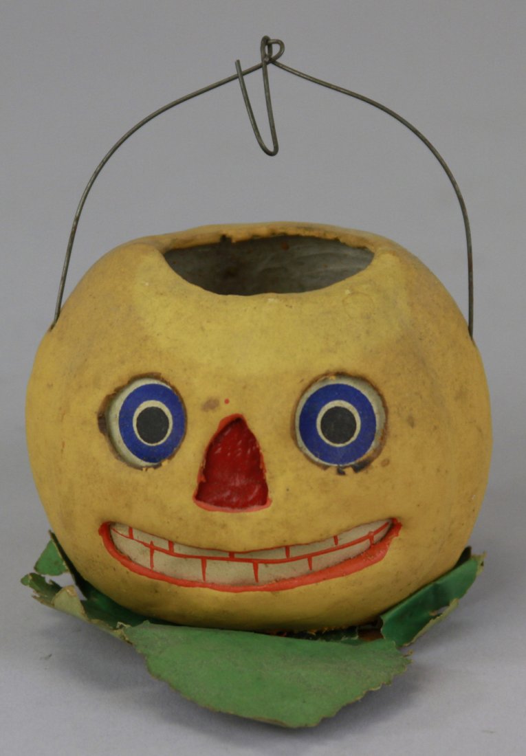 JACK-O-LANTERN CANDY CONTAINER: Germany, composition container done in colorful facial colors, orange overall, paper leaf décor on base, wire handle on top, paper insert for facial features. 2 1/2" h.