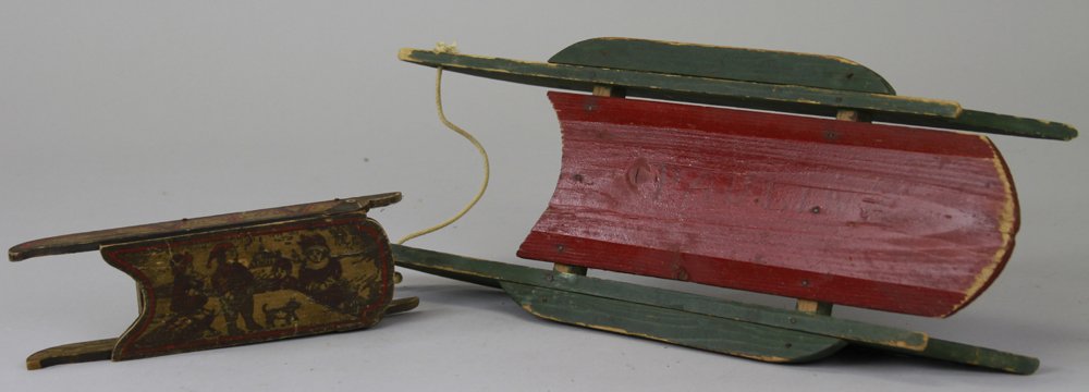 TWO EARLY WOODEN SLEDS: Small wood sled that serves as candy container, decorated with litho children at play in the snow, top swings back to open, along with larger red & green wood doll sled faintly marked "Pauline" on top
