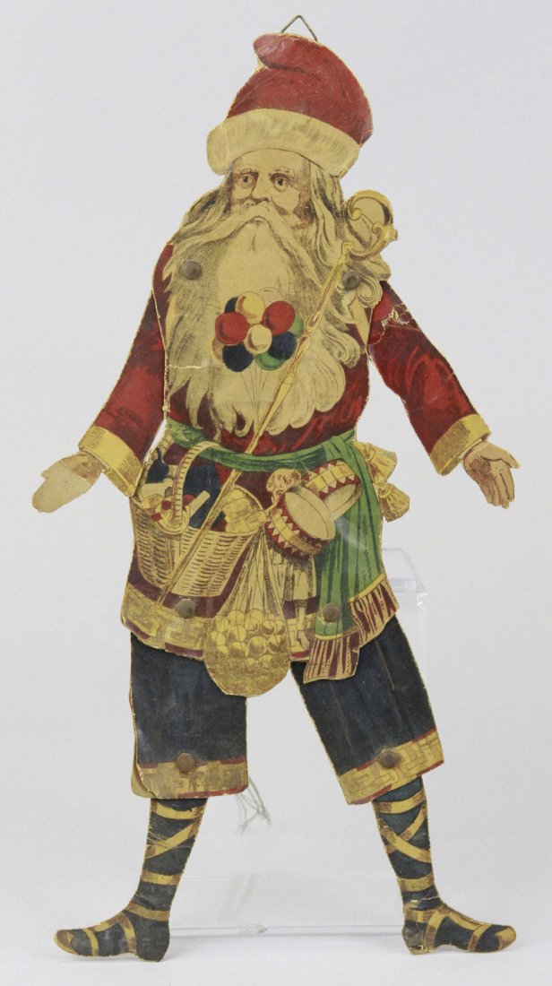 JUMPING JACK SANTA CHRISTMAS TREE ORNAMENT: Early Father Christmas jumping jack, paper litho on cardboard, green sash around waist, wicker basket w/toys, sack of balls, toy drums & dolls hanging from sash, blue culottes & blue boots w/white wra