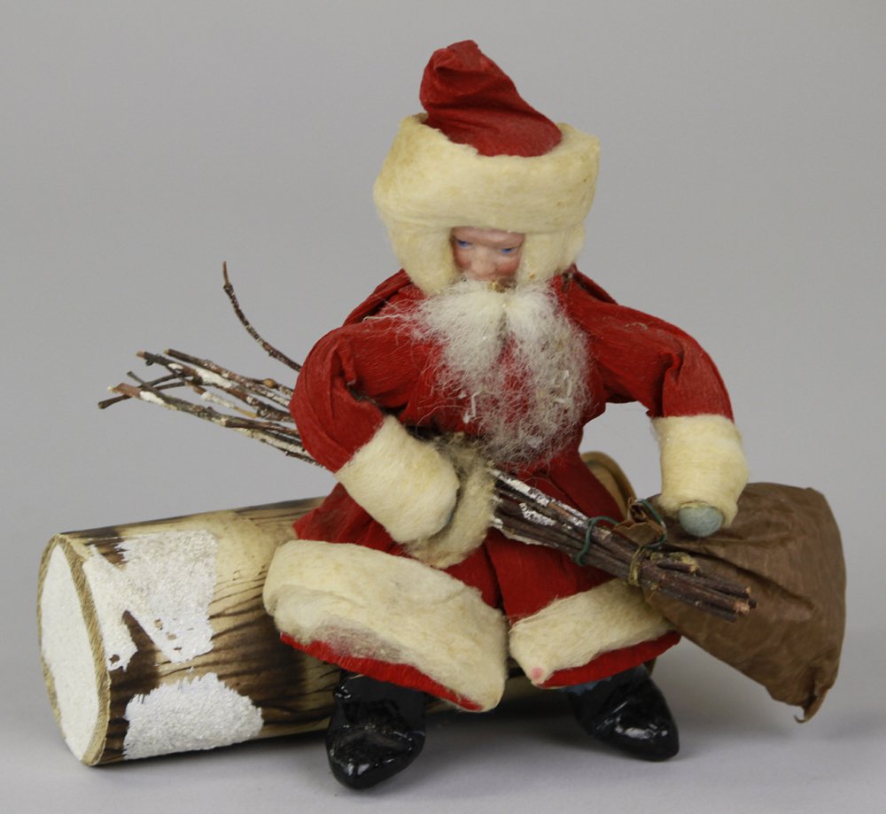 BISQUE FACE GERMAN BELSNICKLE CANDY CONTAINER: Santa sitting on log candy container, dressed in red w/white trim crepe paper over spun cotton, bisque face, holding bag of toys for good children and wood switches to punish bad children, end of log 