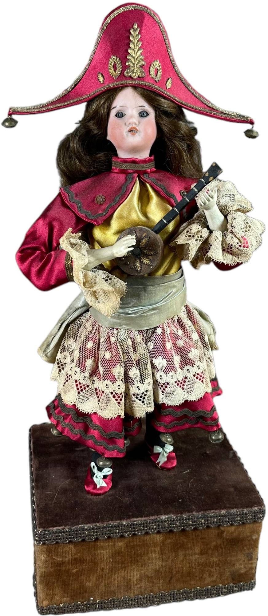 MUSICIAN WITH BICORN HAT AUTOMATON: 1186. MUSICIAN WITH BICORN HAT AUTOMATON | Bisque head and hands musician wearing a bicorn hat. Music plays as she strums her banjo moving arm and twitches wrist slightly for banjo strum. Head moves l