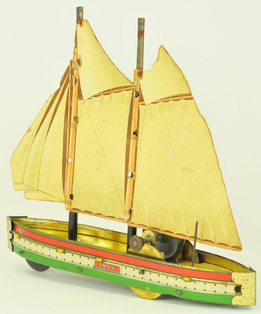 HESS SAILBOAT: Germany, #1045, flywheel powered, lithographed tin, features cardboard sails, nice graphics to cloth sails, hull done in bright red, white, and green, simulated wood deck planking. 11 3/4" l.