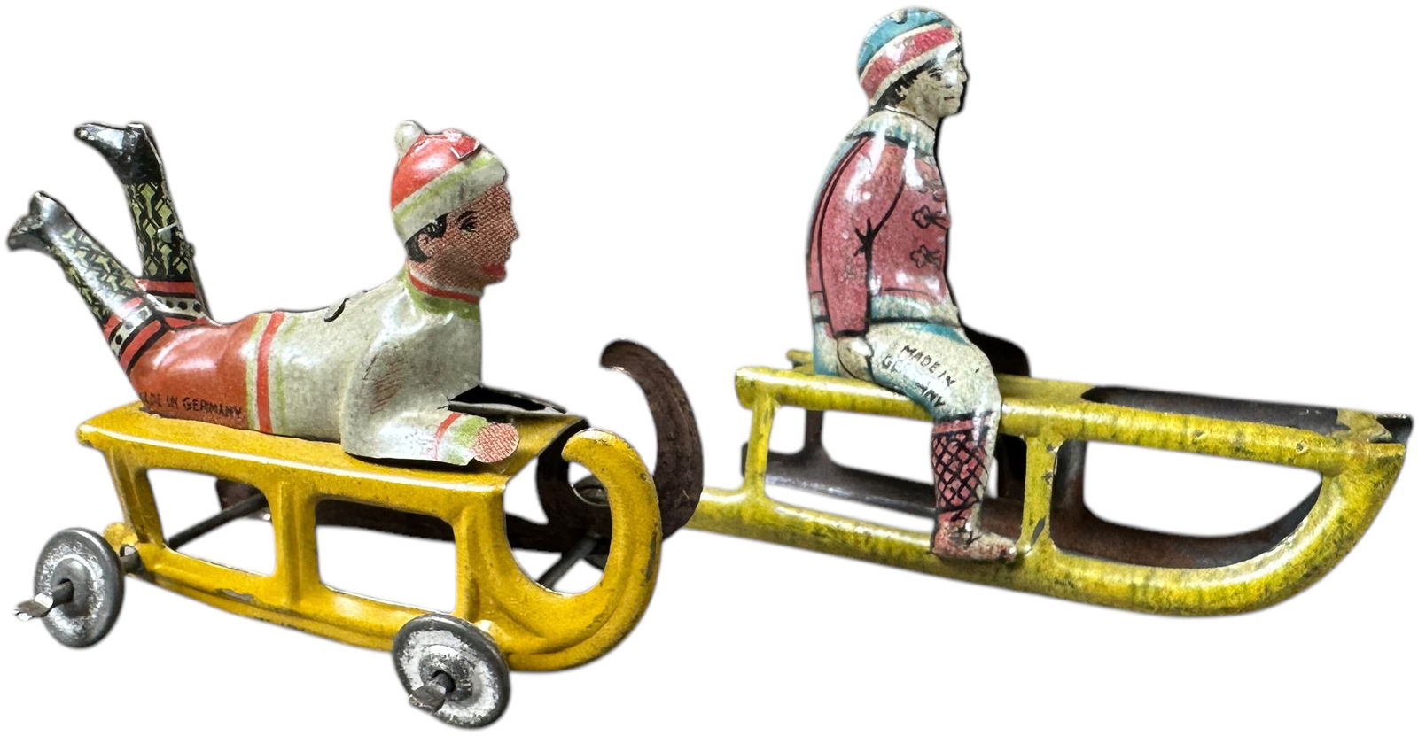 WINTER CHILDREN SLEDDING PENNY TOYS: 303. WINTER CHILDREN SLEDDING PENNY TOYS | Seated child made by Fischer, child on belly made by Meier. | 2.5" l. | (Excellent Condition) | $200 - $400