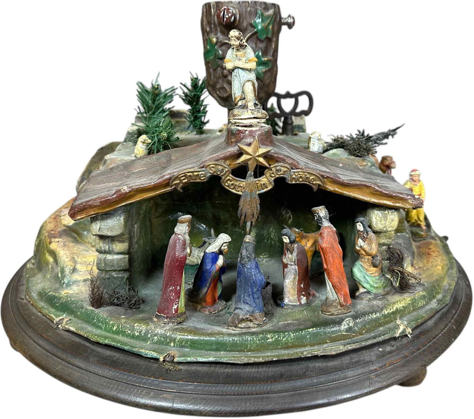 MUSICAL ROTATING TREE STAND W/ MANGER SCENE: 303. MUSICAL ROTATING TREE STAND W/ MANGER SCENE | German Banner reads "Glory to God in the highest", plays different tunes when clockwork wound. Provenance: Bob & Maurine Young | 20" dia. | Common