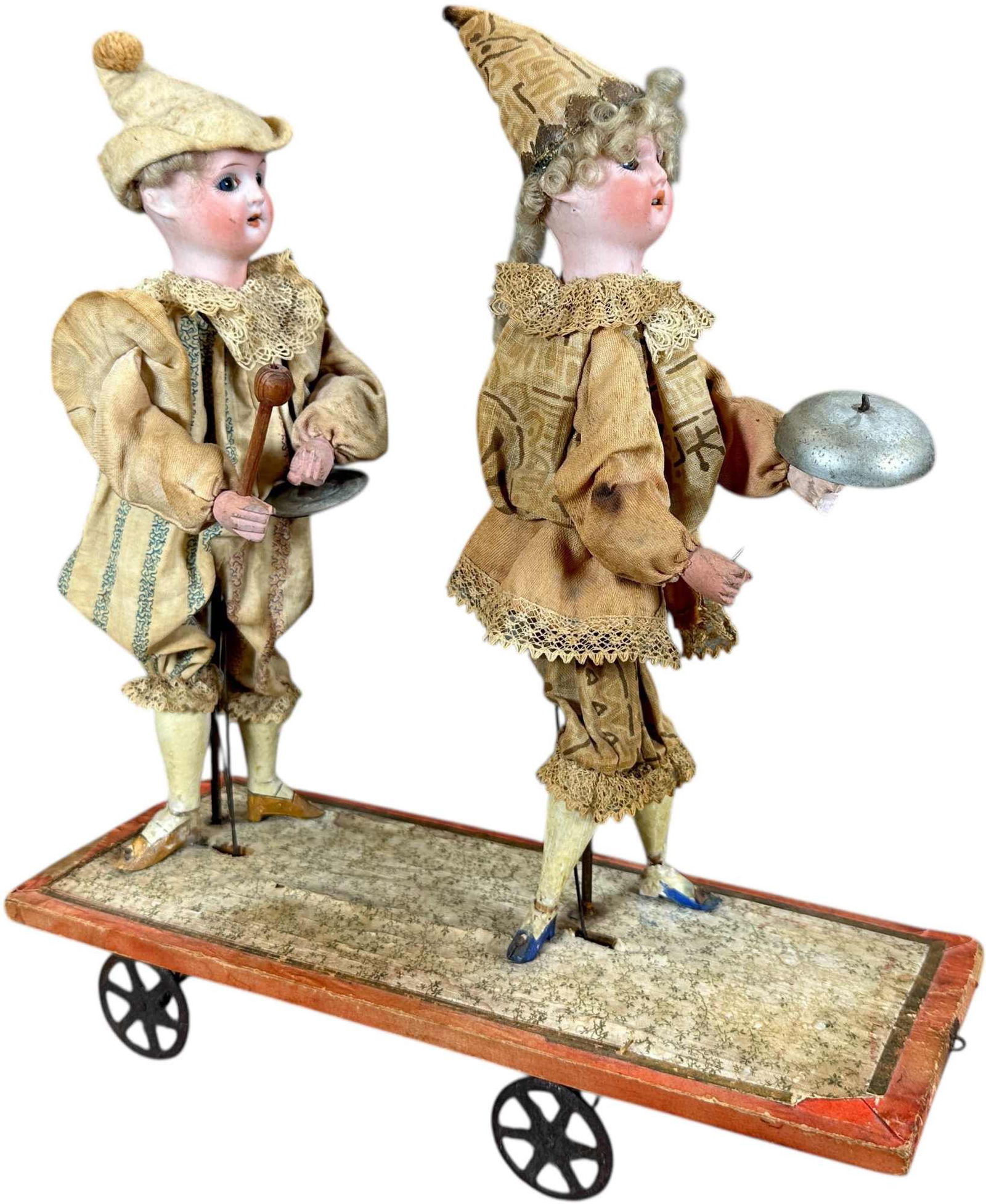 TWO BISQUE HEAD MUSICIANS PULL TOY: 421. TWO BISQUE HEAD MUSICIANS PULL TOY | When pulled along the musicians move their arms as if playing their instruments. | 11" l. | Cracks to two feet, age discoloration to clothes, otherwise