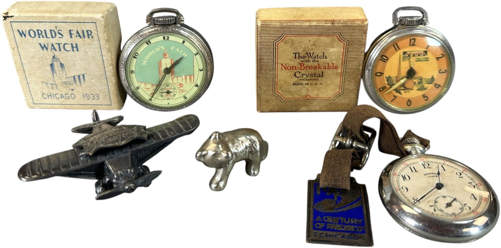 CENTURY OF PROGRESS WATCHES/SOUVENIERS GROUPING: 43. CENTURY OF PROGRESS WATCHES/SOUVENIERS GROUPING | Includes three watches, small plane and bear. | 2" l. | One watch sluggish, (Excellent Condition) | $250 - $500