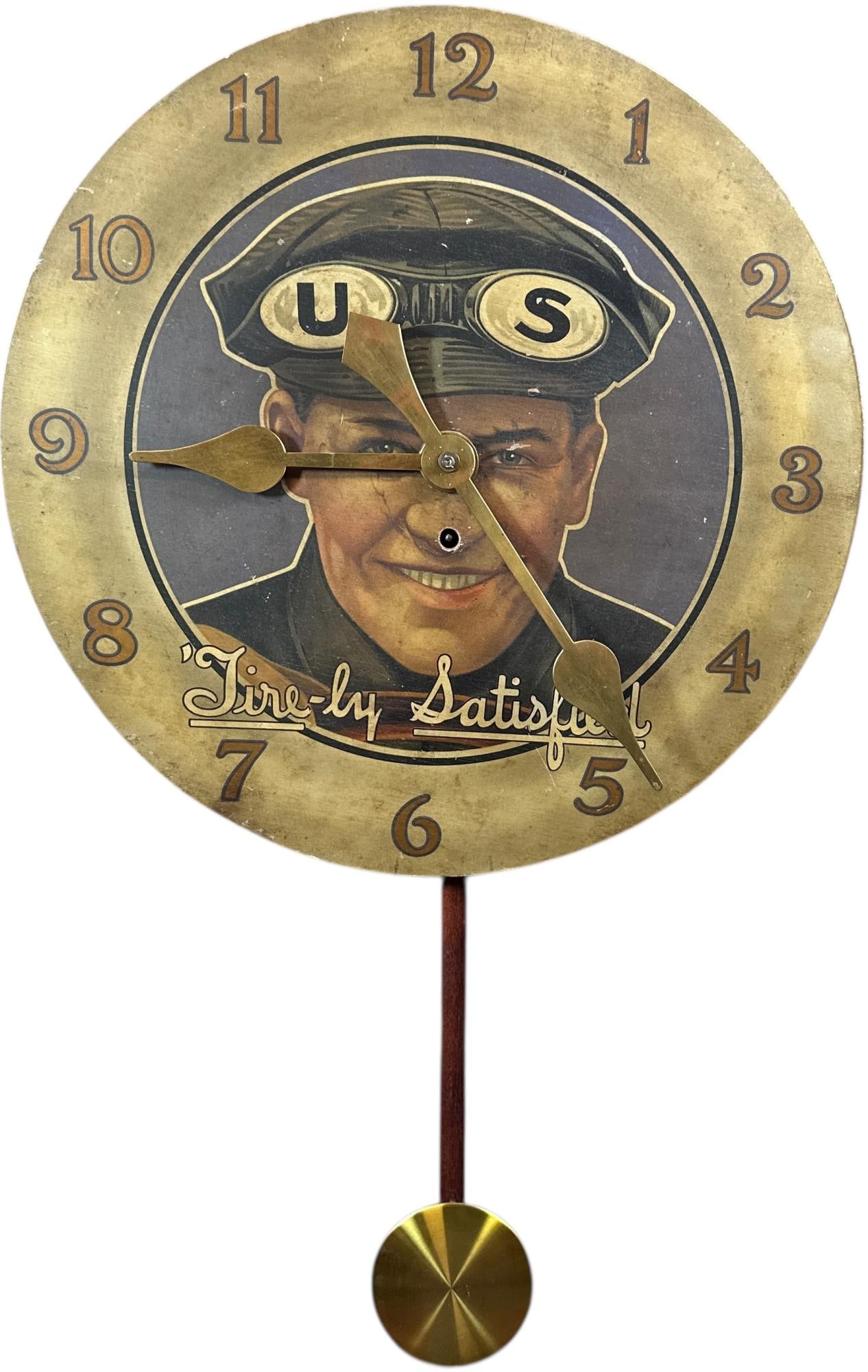 US TIRE ADVERTISING WALL CLOCK: 105. US TIRE ADVERTISING WALL CLOCK | Featuring the iconic "Tire-ly Satisfied" service attendant portrait beneath a brass-tone numeral dial with matching hands and pendulum. A premier automotive adver