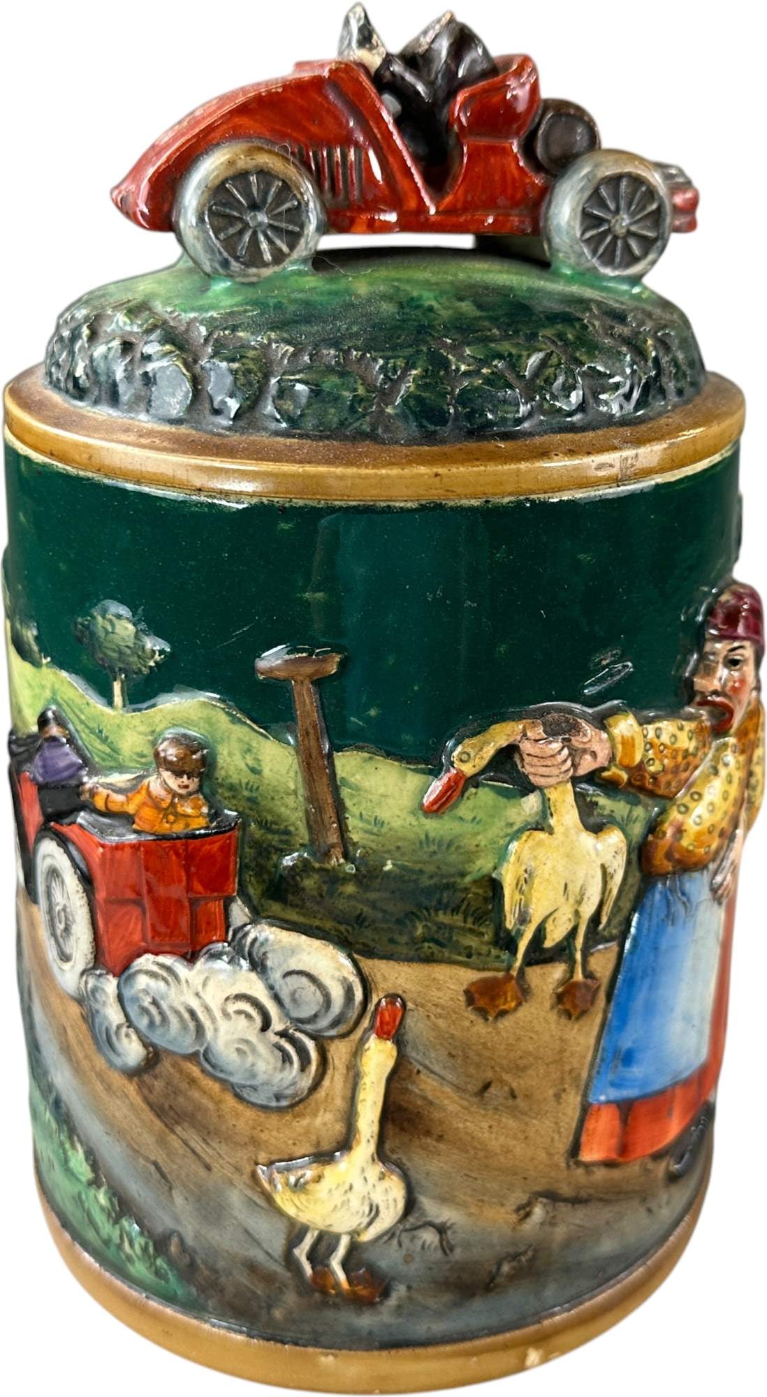 EMBOSSED GERMAN TOBACCO JAR: 400. EMBOSSED GERMAN TOBACCO JAR | Handpainted comical automotive scene on earthenware. From the David Bausch Automobilia Collection. | 8.5" h. | Driver's head missing, small chip in lid rim, otherwis