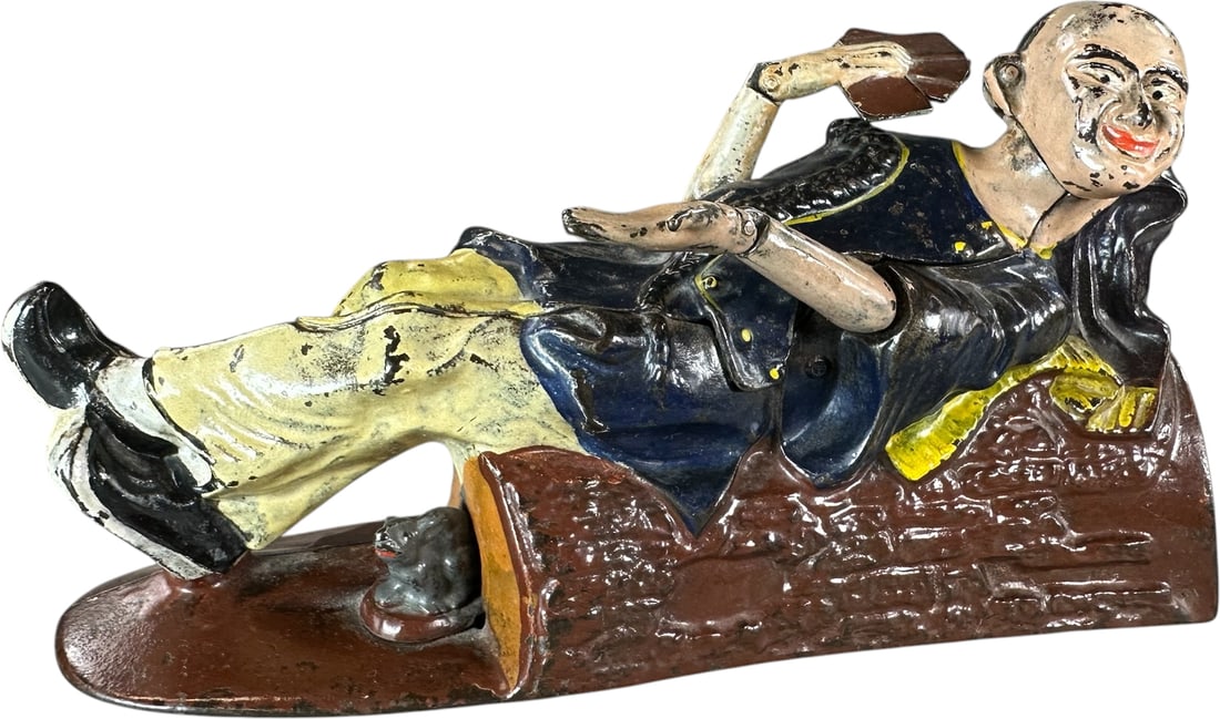 RECLINING CHINAMAN MECHANICAL BANK: 10. RECLINING CHINAMAN MECHANICAL BANK | J&E Stevens Co., scarce bank with a great deposit action when activated. Provenance: The Robert Booth Jr. Collection. | 8.5" l. | Free from repaints or replace