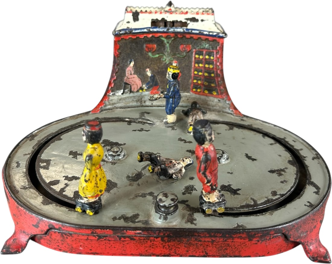 ROLLER SKATING RINK MECHANICAL BANK: 27. ROLLER SKATING RINK MECHANICAL BANK | Kyser & Rex Co., a sought after bank which commands attention on the shelf, the coin is placed on roof and pressing lever allows skaters to glide around to re