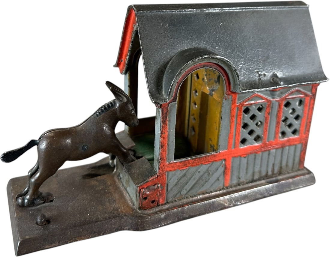 MULE ENTERING BARN MECHANICAL BANK: 87. MULE ENTERING BARN MECHANICAL BANK | J&E Stevens Co. Provenance: The Robert Booth Jr. Collection. | 8.5" l. | Tail is the common replacement piece, otherwise all original and free from cracks in (
