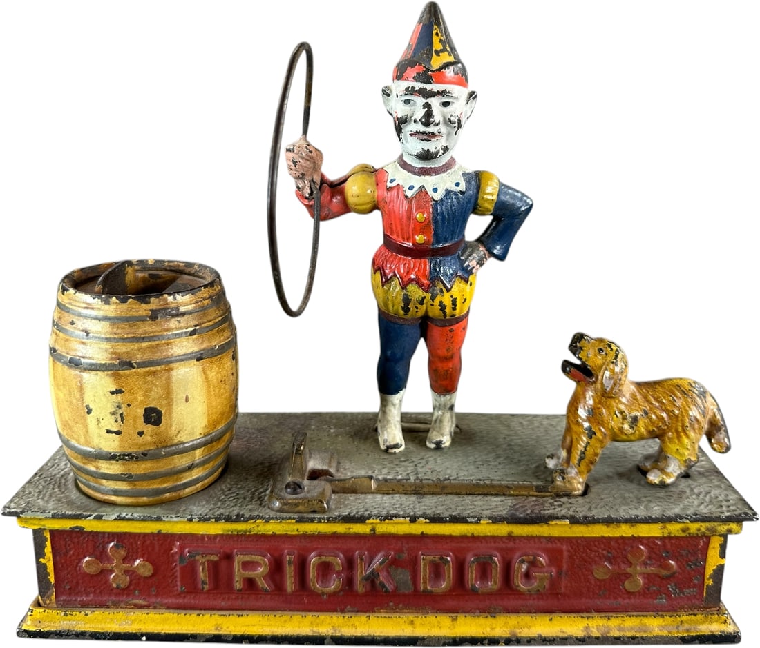 TRICK DOG MECHANICAL BANK: 96. TRICK DOG MECHANICAL BANK | Shepard Hardware Co. Provenance: The Robert Booth Jr. Collection. | 9" l. | Clown figure is partially overpainted and glued at ankles otherwise displaying in (Very