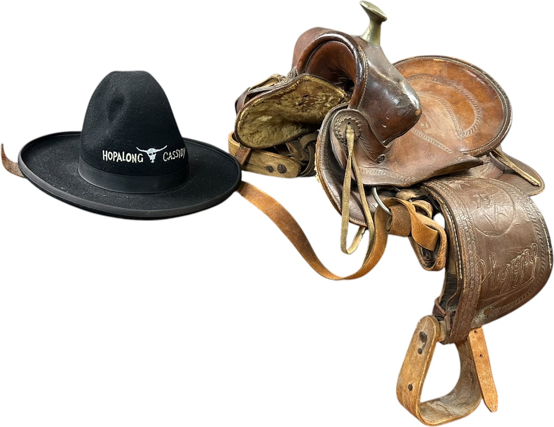 HOPALONG CASSIDY SADDLE & COWBOY HAT: 36. HOPALONG CASSIDY SADDLE & COWBOY HAT | Vintage childs Western saddle with tooled leather decoration, wooden stirrups and embossed Hopalong Cassidy name and portrait on the fender, along with a bla