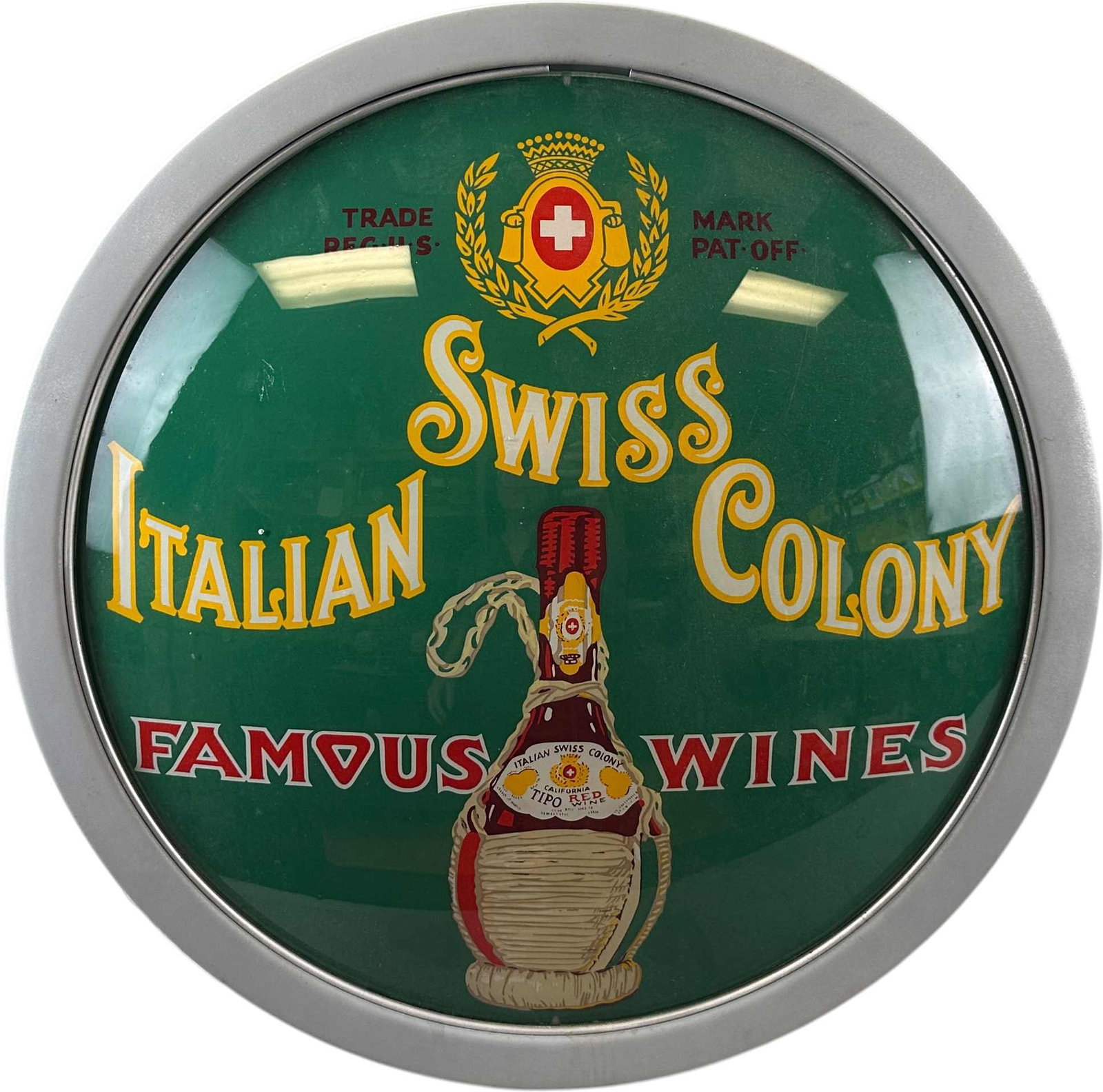SWISS ITALIAN COLONY WINES ILLUMINATED SIGN: 73. SWISS ITALIAN COLONY WINES ILLUMINATED SIGN | Round glass-faced advertising sign for Italian Swiss Colony Famous Wines, featuring a green field with the company crest and illustrated bottle of Tip