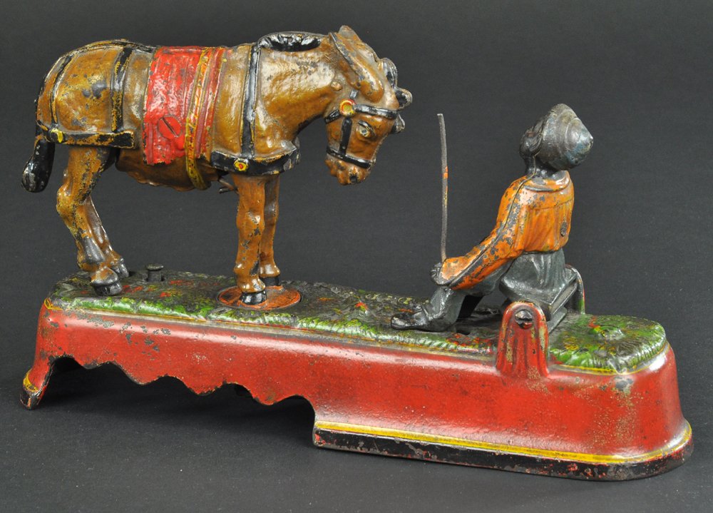 I SPIZE A MULE BENCH MECHANICAL BANK: Orange shirt, J & E Stevens Co., designed by James H. Bowen, patented 4/27/1897. When the mule and boy are brought into position, a slight touch on the knob at the base causes the mule to turn around
