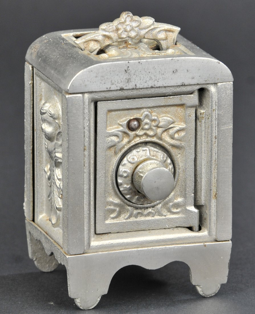 CUPID SAFE STILL BANK: Cast iron, Kenton, c. 1911, nickeled finish safe features cupids embossed on sides extendable top handle at top, combination lock. 4 5/8"h.