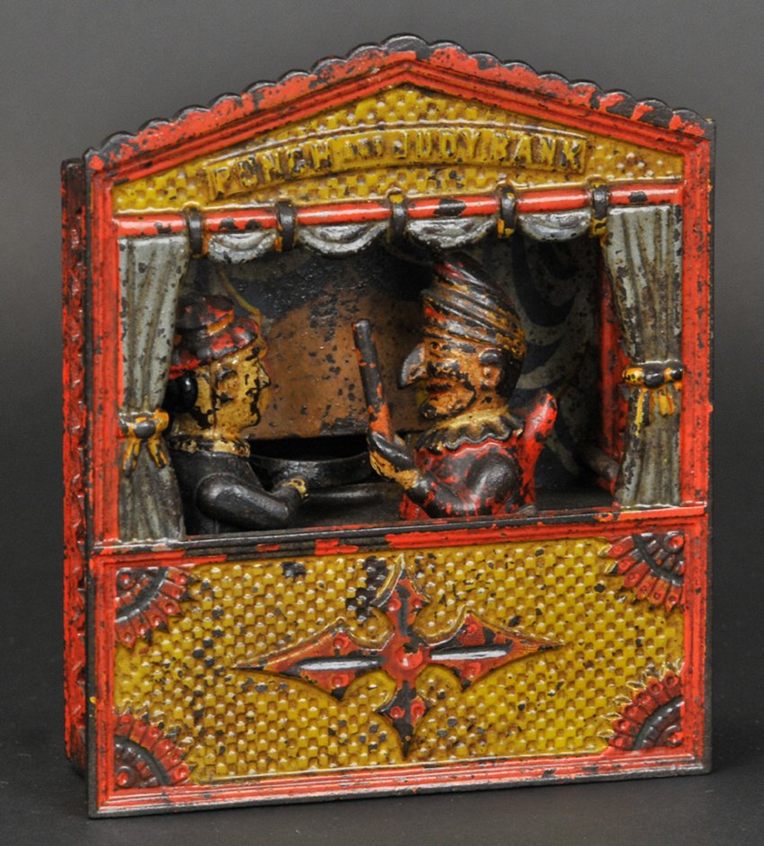 PUNCH AND JUDY MECHANICAL BANK (MEDIUM LETTERS): Shepard Hardware Co., designed by Peter Adams & Charles Shepard, patented 7/15/1884. Judy receives the coin in the plate, the thumb piece at the side is pressed upon and Punch rushes forward brandishi