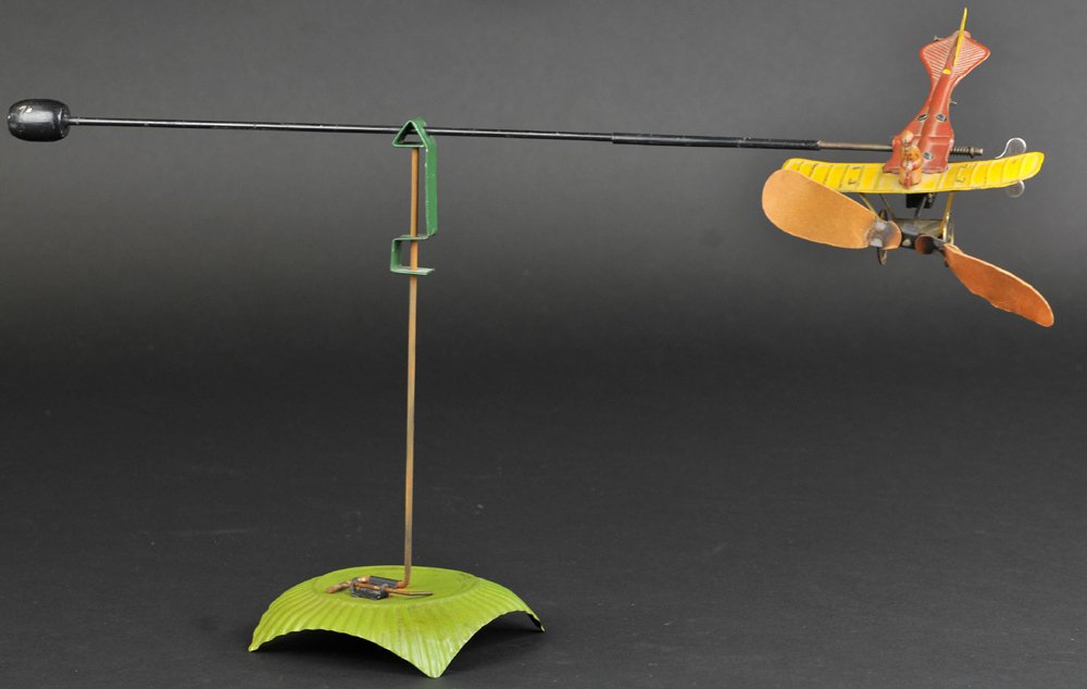 CIRCLING AIRPLANE ON BASE: Distler, Germany, tinplate toy monoplane with wing mounted pilot and clockwork driven props able to fly around base and roll as it makes a circling motion. Airplane 6" l. Support bar 16" overall