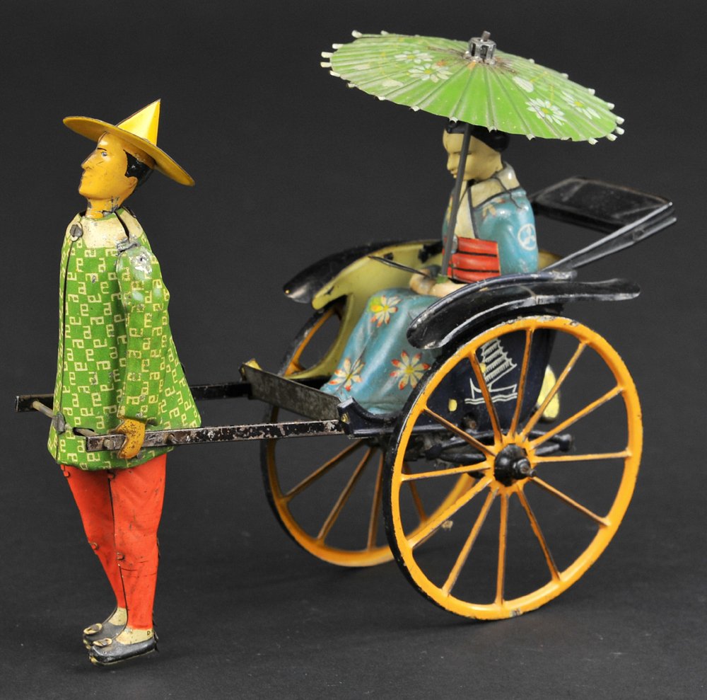 LEHMANN MASUYAMA: Germany, depicts lithographed tin rickshaw pulled by standing figure while woman holding floral designed parasol is seated in spoked carriage, clockwork driven. 6 3/4" l.