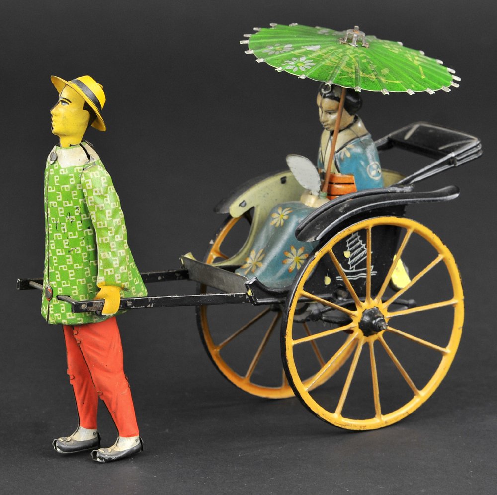 LEHMANN MASUYAMA: Germany, depicts lithographed tin rickshaw pulled by standing figure while woman holding floral designed parasol is seated in spoked carriage, clockwork driven. 6 3/4" l.