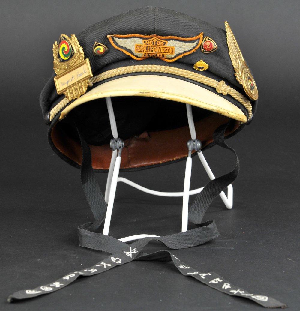 1950's HARLEY DAVIDSON HAT WITH MEDALLIONS: Classic black hat with white brim, Harley patch on front, contains 1957 "GYPSY TOUR" badge, 1950 "AMA TOUR AWARD" badge with name, along with smaller pins, (VG Cond.) Hat size 6 7/8.