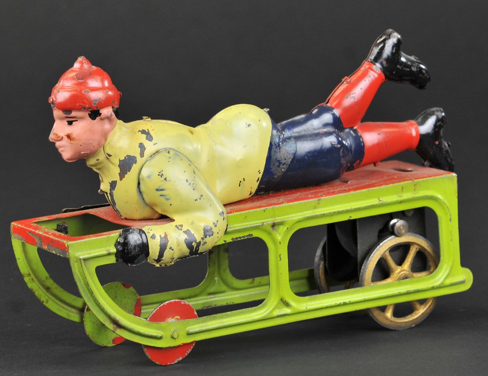 DAYTON BOY ON SLED: Pressed steel, friction driven, colorful example overall, figure done in multi-painted clothes, green sled, depicted with hands on sides, and legs in upright pose. 9" l.