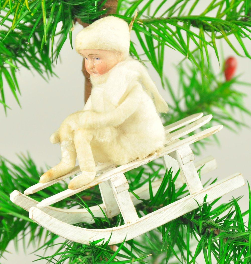 BISQUE HEAD GIRL ON SLED: Germany, pressed cotton child with bisque head on wood sled Christmas tree ornament, playful design. 3" l.