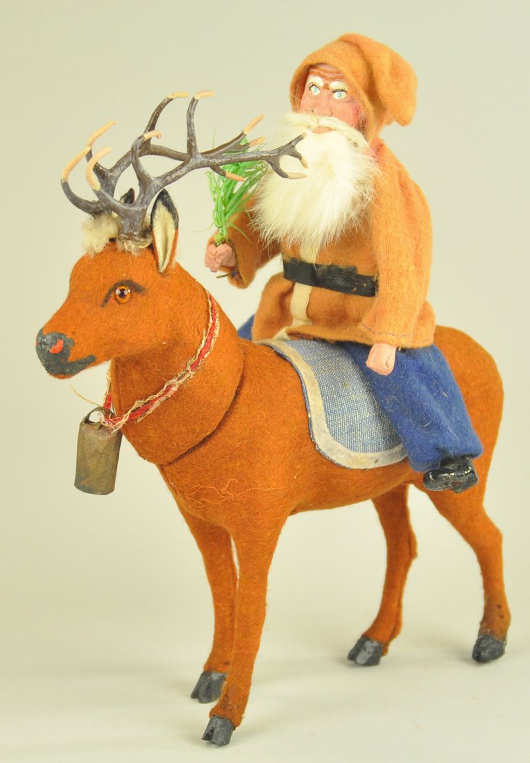 SANTA ON REINDEER CANDY CONTAINER: Composition Santa with red felt robe and blue pants, rabbit fur beard, mounted on pressed cardboard, reindeer covered in felt with glass eyes, metal antlers and cow bell around his neck, head removes 