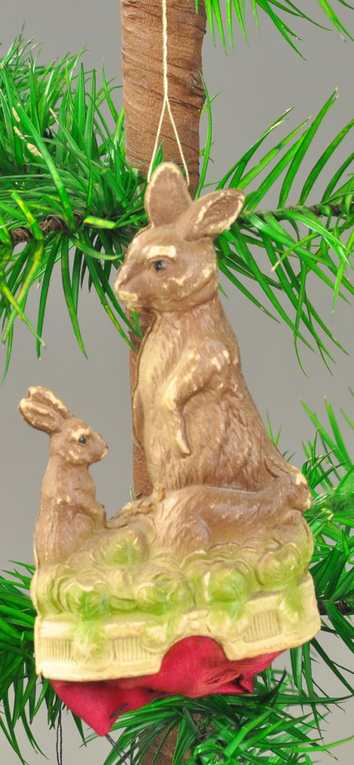 MOMMA RABBIT & BABY BUNNY CANDY CONTAINER: Germany, Dresden red silk bag candy container with mother and baby rabbit sitting on cabbage patch base. 3 1/4" l. Ex. Tom Fox Collection.