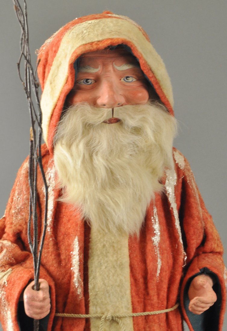 LARGE EARLY FATHER CHRISTMAS CANDY CONTAINER: This hard to fine large example is wearing a long red robe with mica flecked patches of snow, two pockets to hold Christmas toys, a well detailed composition face with rabbit fur beard, cornucopia can