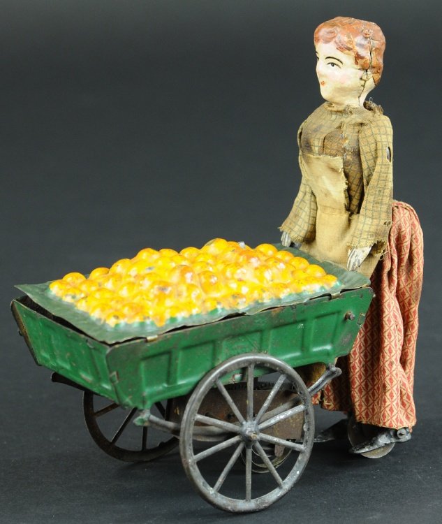 ORANGE VENDOR: Fernand Martin, France, hand painted tin figure of woman wearing cloth dress and pushing spoke wheeled wagon with embossed load of fresh oranges, clockwork driven. 6 1/2" l.