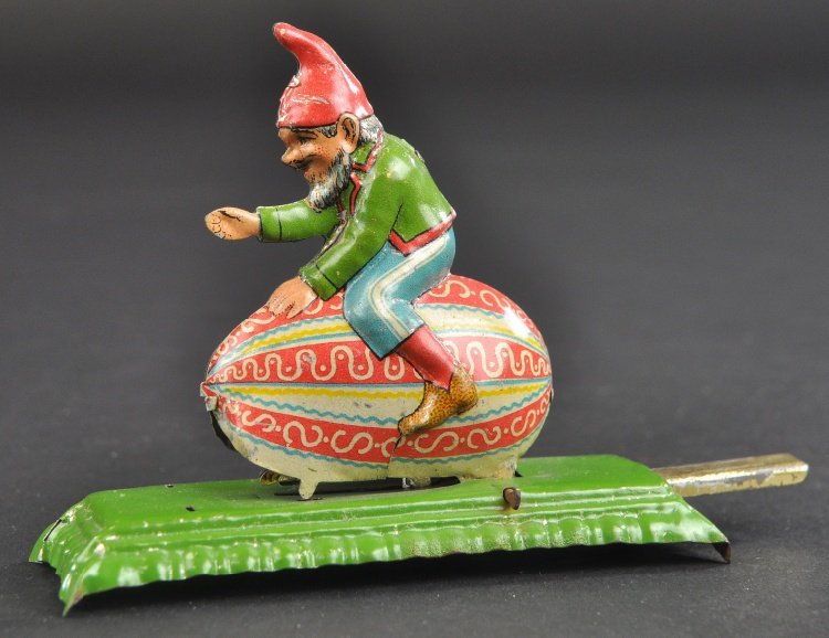 GNOME ON EGG ARTICULATED PENNY TOY: Meier, colorful lithographed tin, depicts gnome riding decorated egg, when plunger is pressed a bunny appears from under the egg. 3" l.