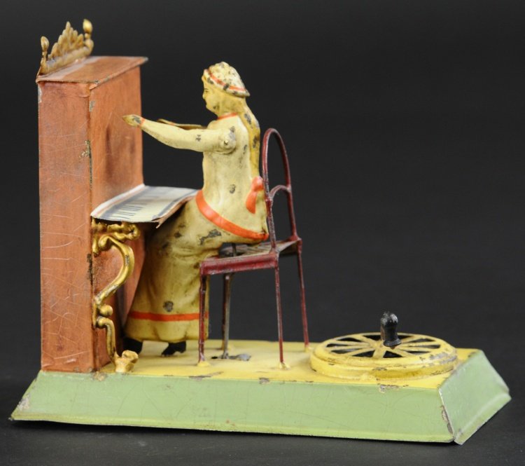 GIRL AT PIANO MECHANICAL TOY: Germany, attributed to Bing, hand painted tin, depicts young woman seated on chair at upright piano, turn handle on base causes arms to rise as plink-plink sounds are emitted. 5 1/2" h x 6 1/2" l.