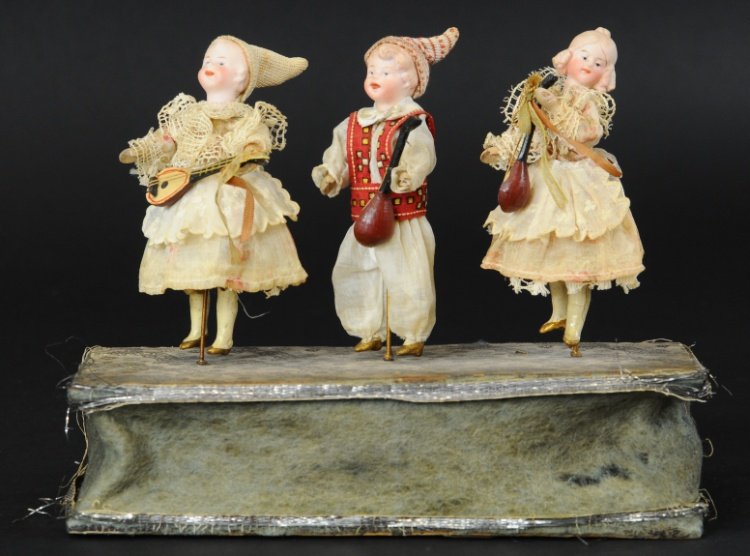 MECHANICAL BISQUE HEAD DANCERS: Squeak box base, an exquisite toy featuring three children in cloth attire, each holding mandolin in hand, squeezing toy causes body movements.